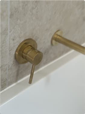 Brass wall-mounted bath mixer installed on stone tile